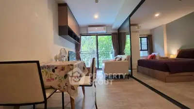 Modern studio apartment with open layout, cozy dining area, and large windows offering lush green views.