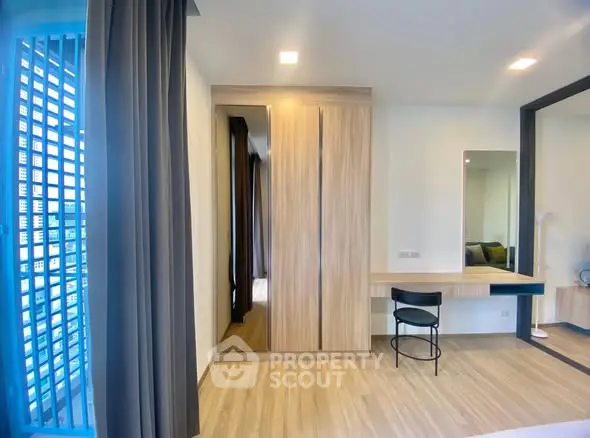 Modern bedroom with wooden wardrobe and sleek desk, featuring large windows for natural light.