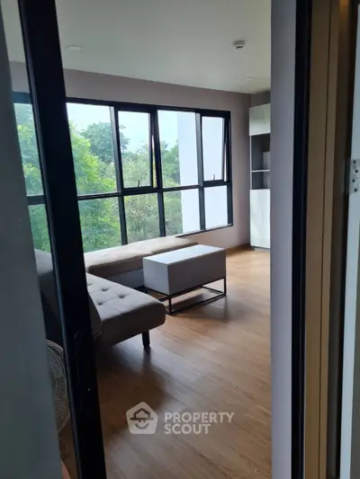 Modern living room with large windows and stylish furniture, offering a serene view of lush greenery.