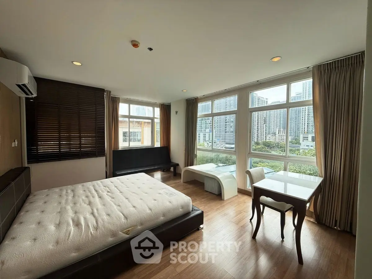 Spacious bedroom with large windows offering stunning city views, featuring modern furniture and elegant decor.