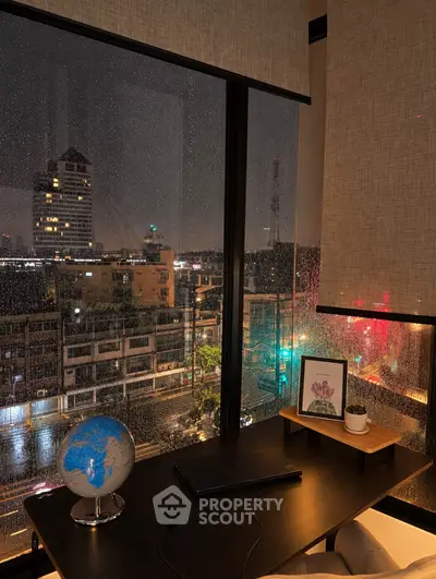 Cozy study room with night city view through large window, featuring a desk with globe and framed art.