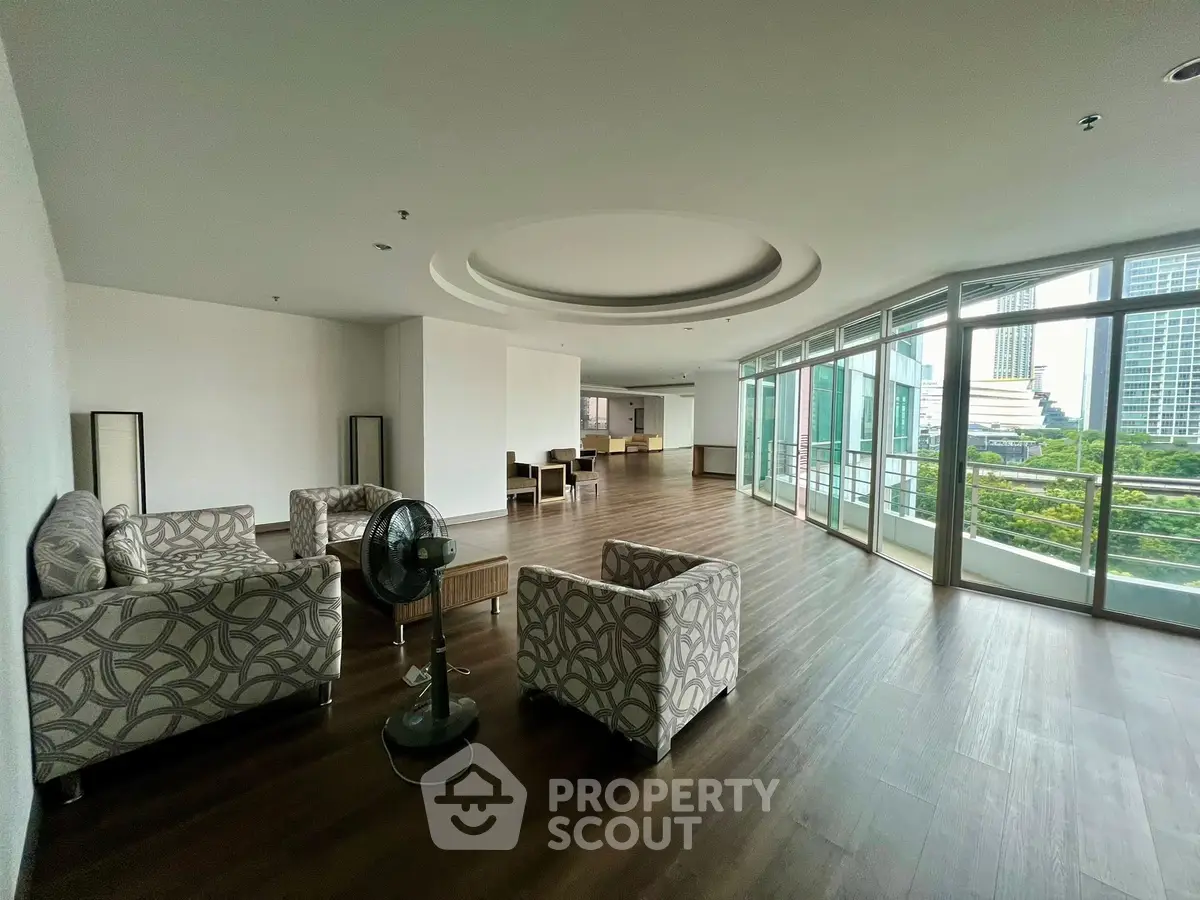Spacious modern living room with large windows and city view, featuring stylish furniture and elegant wood flooring.