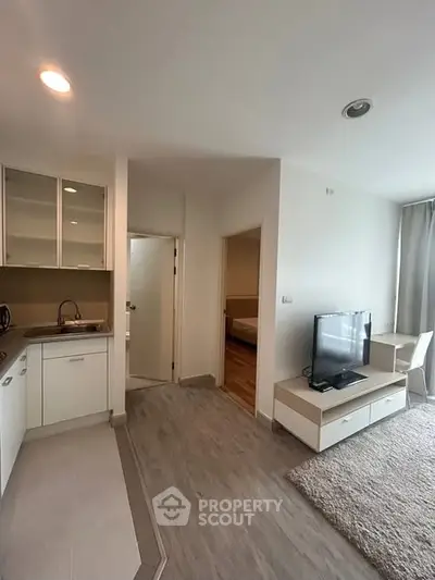 Modern open-plan living room with kitchen and TV area, featuring sleek design and natural lighting.