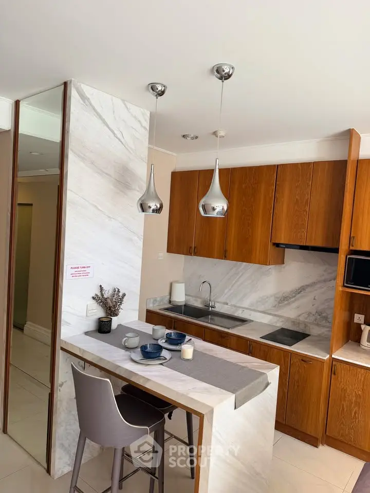 Modern kitchen with sleek wooden cabinets and marble countertops, featuring stylish pendant lighting and breakfast bar.