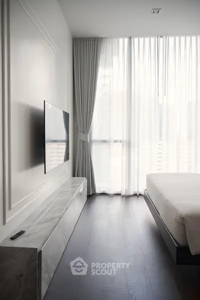 Modern bedroom with sleek TV setup and floor-to-ceiling windows for natural light.