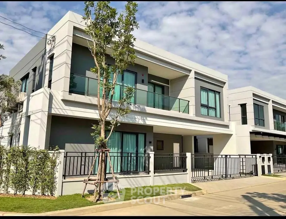 Modern two-story house with large windows and balcony in a suburban neighborhood.