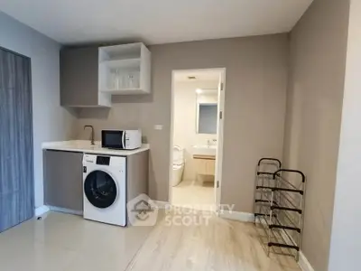 Modern apartment with compact kitchen and bathroom view, featuring washing machine and microwave.