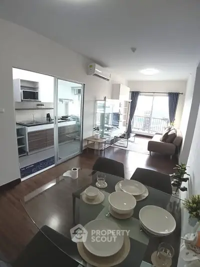 Modern open-plan living room with dining area and kitchen, featuring sleek furniture and large windows.