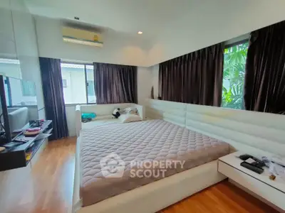 Spacious bedroom with large windows and modern decor, featuring a comfortable bed and hardwood flooring.