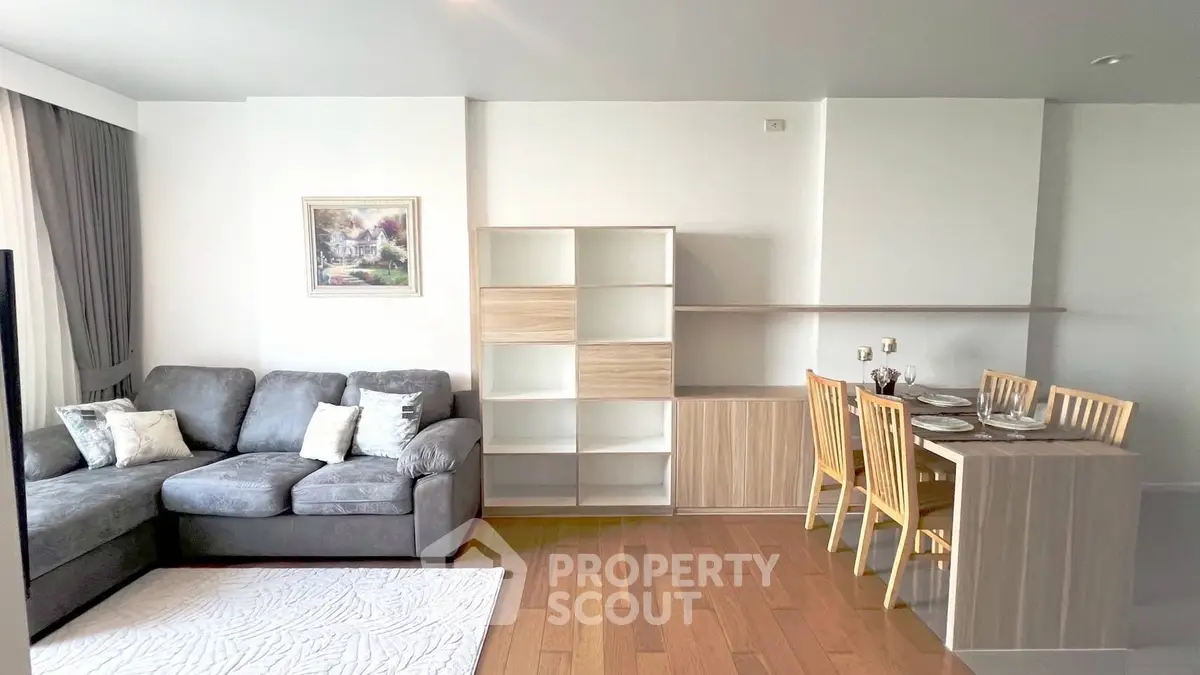 Modern living room with cozy gray sofa, elegant dining area, and stylish shelving unit.