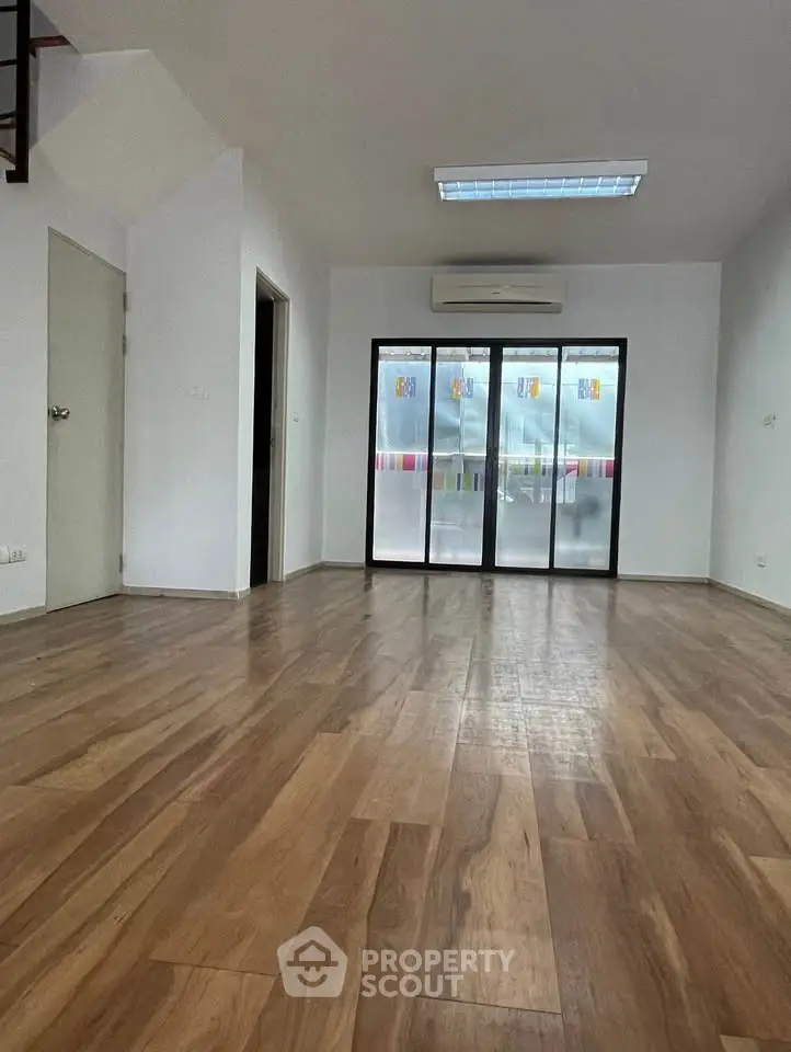 Spacious empty room with wooden flooring and large windows, perfect for customization.