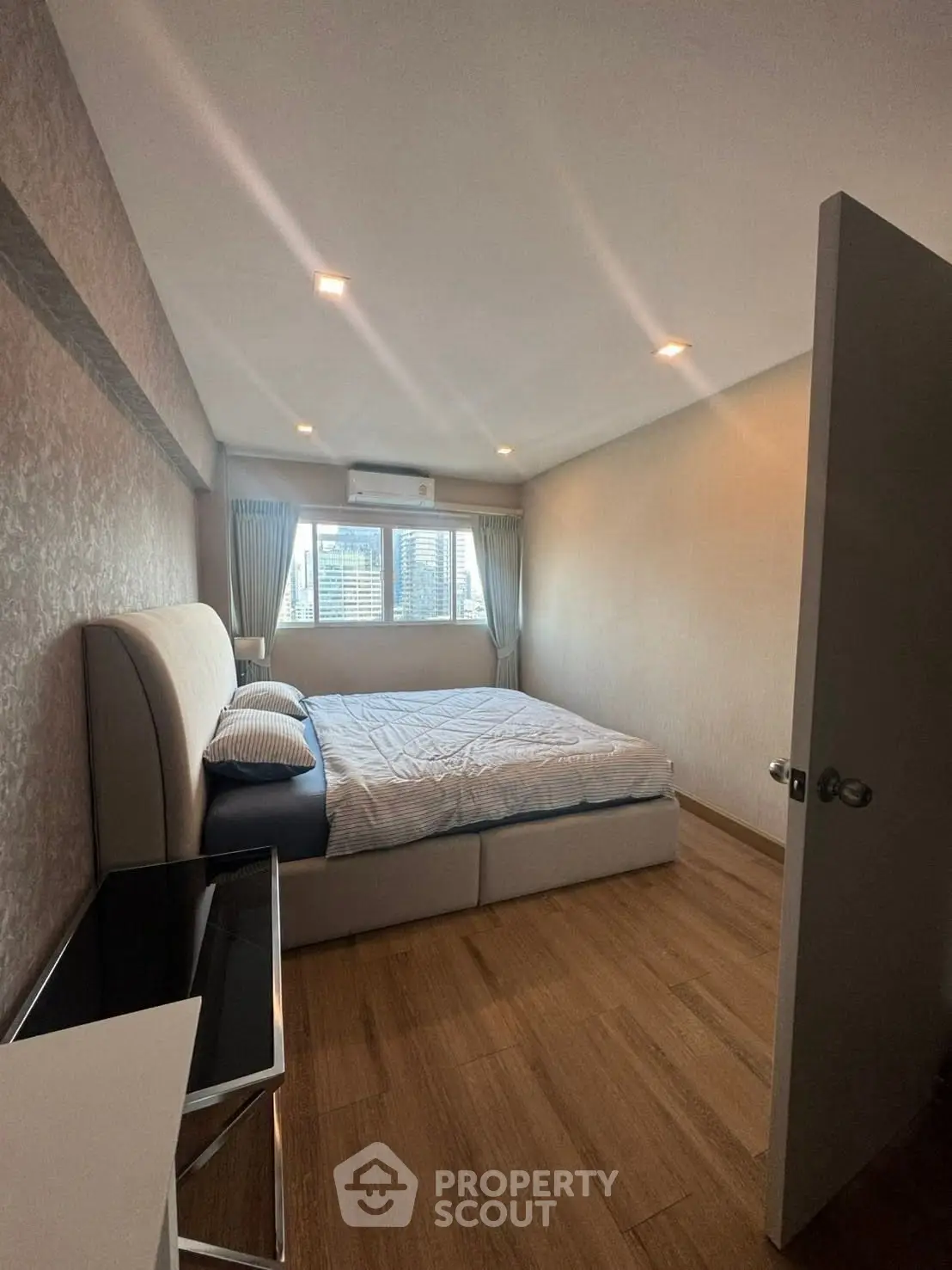Spacious bedroom with modern decor and large window offering city views.