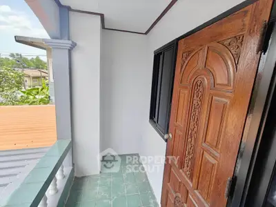 Charming small balcony with wooden door and green tile flooring, perfect for relaxation.