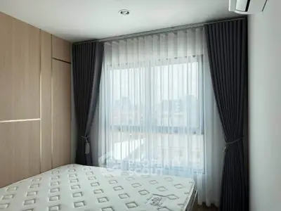 Modern bedroom with large window and stylish curtains, featuring a comfortable mattress and sleek wooden wardrobe.