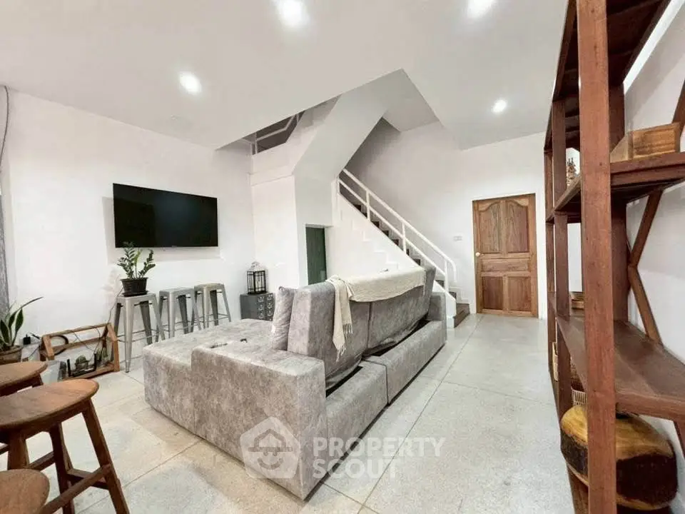Modern living room with stylish gray sofa and wall-mounted TV, featuring open staircase and wooden accents.