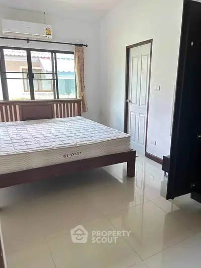 Spacious bedroom with large window and modern furnishings in a serene residential area.
