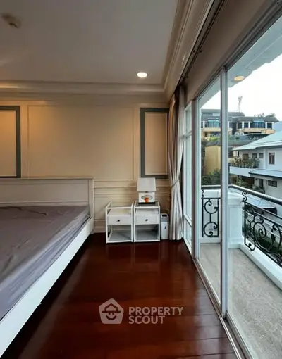 Spacious bedroom with balcony offering scenic views of surrounding buildings.