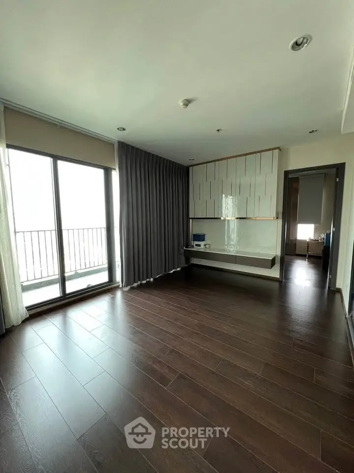 Spacious modern living room with wooden flooring and large windows leading to a balcony.
