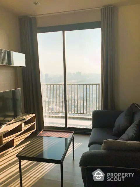 Sunlit modern living room with expansive city views through floor-to-ceiling windows, complemented by a cozy sofa and sleek entertainment unit.