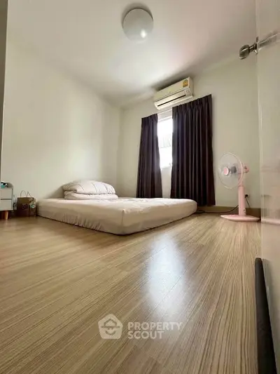 Minimalist bedroom with wooden flooring and air conditioning, featuring a low bed and modern decor.