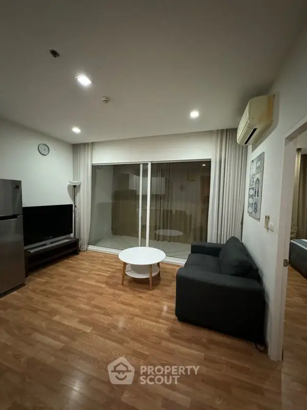 Spacious living room with polished hardwood floors, modern furniture, and ample natural light from large sliding glass doors leading to a cozy balcony.