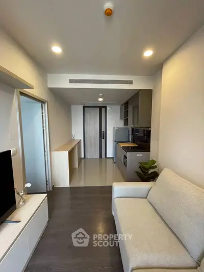 Modern living room with sleek kitchen, cozy sofa, and stylish decor in a compact apartment.