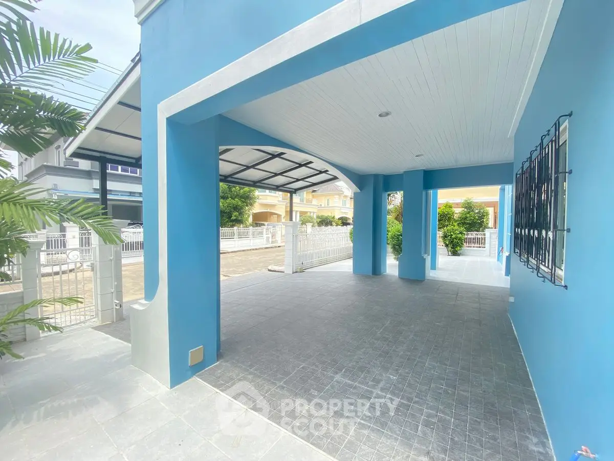 Spacious covered parking area with modern blue exterior and lush greenery.