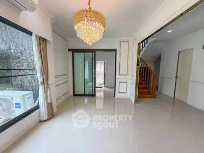 Spacious living room with elegant chandelier and large window, featuring modern sliding doors and polished flooring.