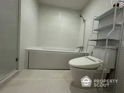 Modern bathroom with sleek white tiles and bathtub, featuring a contemporary toilet and shelving unit.