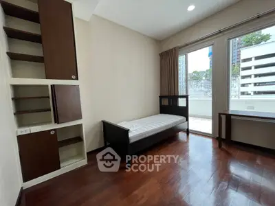 Spacious bedroom with wooden flooring and large window access to balcony in modern apartment.