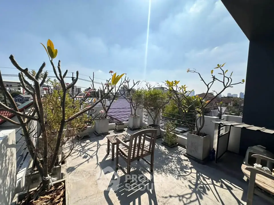 Charming rooftop terrace with potted plants and seating, offering a serene urban view under a clear blue sky.