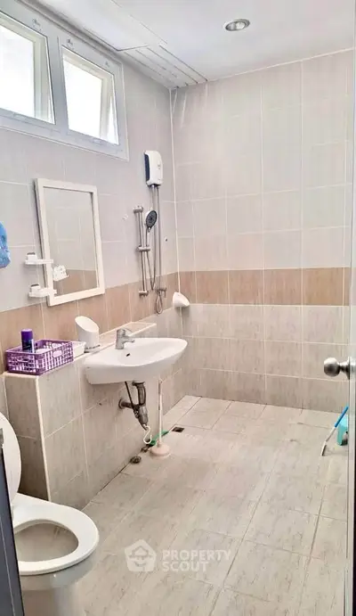 Modern bathroom with sleek design and neutral tiles, featuring a shower and contemporary fixtures.