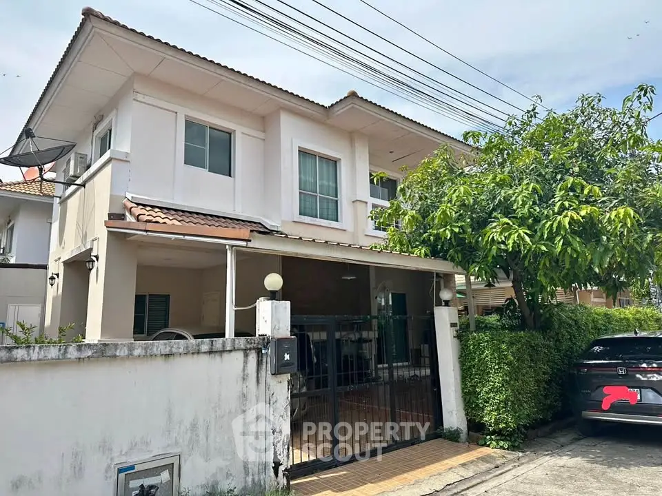 Charming two-story house with gated entrance and lush greenery in a serene neighborhood.