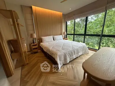 Spacious bedroom with large windows and serene forest view, featuring elegant wooden flooring and modern decor.