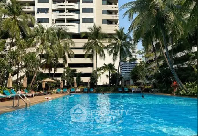 Luxurious residential building with a stunning outdoor pool surrounded by palm trees and sun loungers.