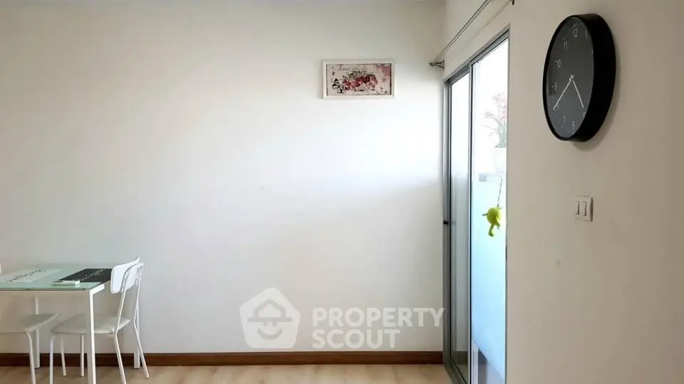 Minimalist dining area with wall clock and sliding glass door to balcony.