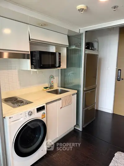 Modern compact kitchen with washing machine and microwave in sleek apartment.