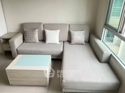 Modern living room with stylish gray sectional sofa and sleek coffee table by large window.