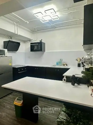 Modern kitchen with sleek black cabinets and white countertops, featuring built-in appliances and stylish lighting.