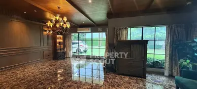 Luxurious living room with marble flooring and large windows overlooking a garden, featuring elegant lighting.