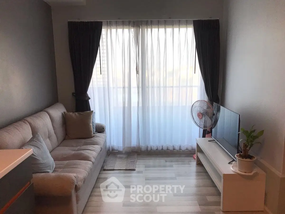 Cozy living room with modern sofa and TV, featuring large window with curtains.