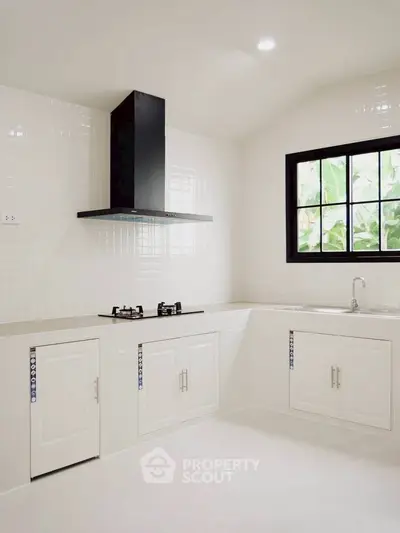 Modern kitchen with sleek white cabinetry and gas stove, featuring a large window for natural light.