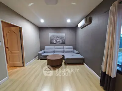 Modern living room with sleek grey sofa and wooden flooring, featuring elegant lighting and air conditioning.