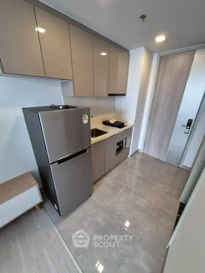Modern kitchen with sleek cabinets and stainless steel fridge in compact layout.
