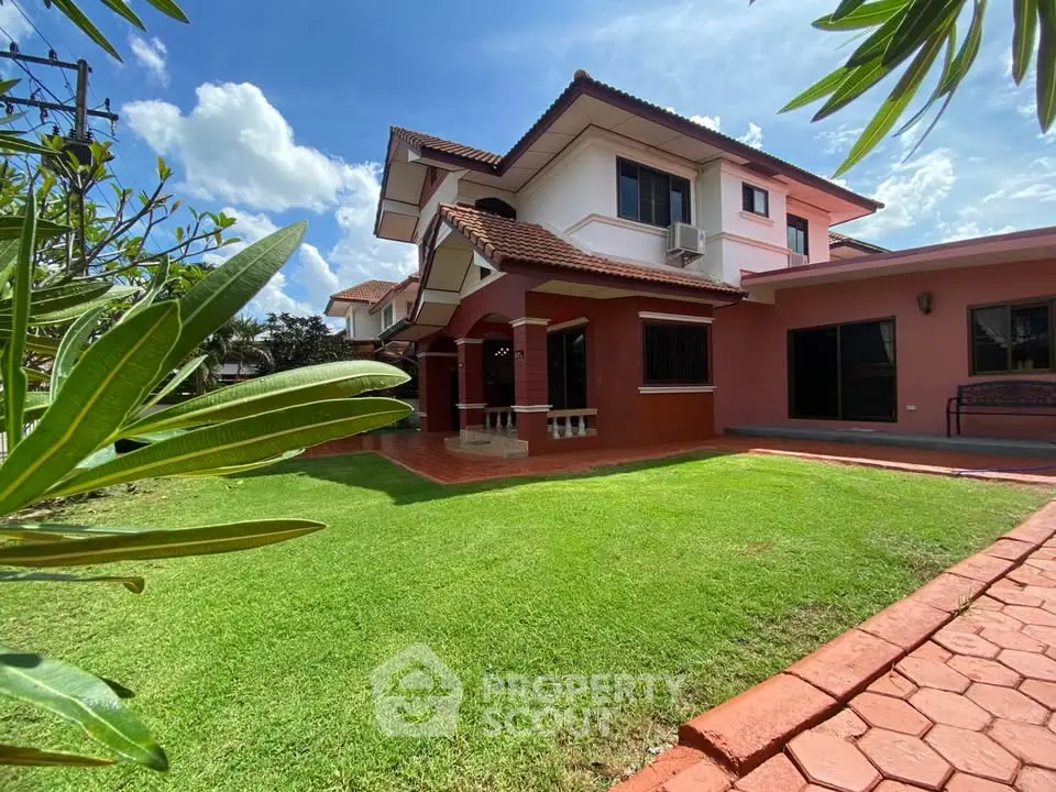 Charming two-story house with lush garden and red brick pathway under a clear blue sky.