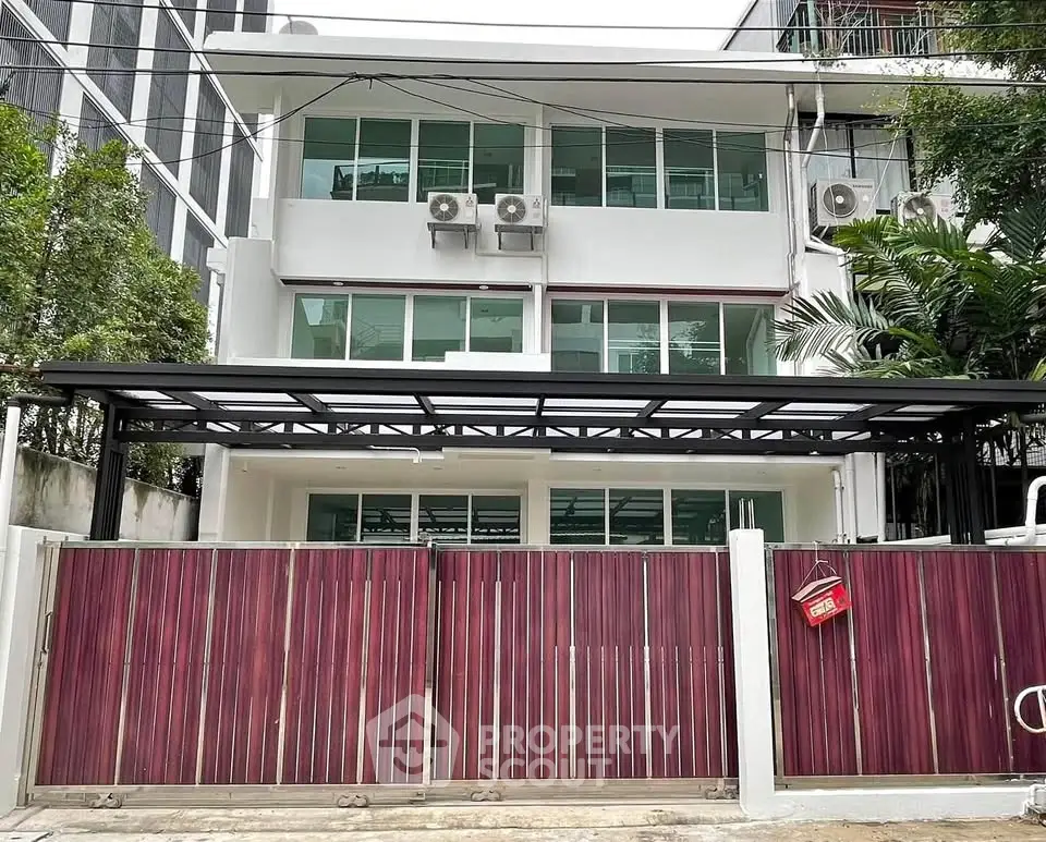 Modern three-story building with gated entrance and lush greenery in urban setting
