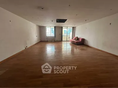 Spacious empty living room with wooden floors and large windows offering city views.