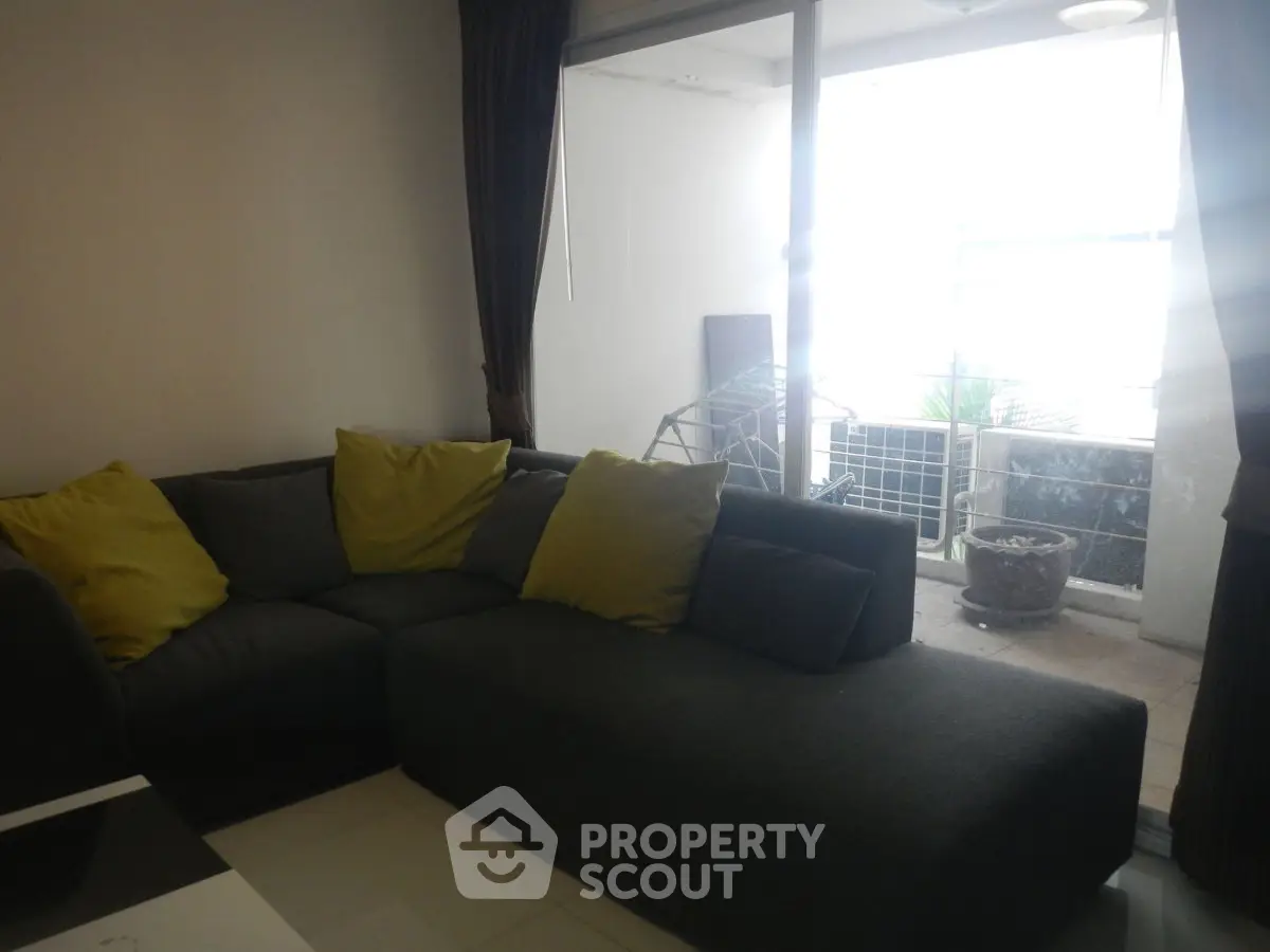 Cozy living room with modern sofa and access to a bright balcony, perfect for relaxation.