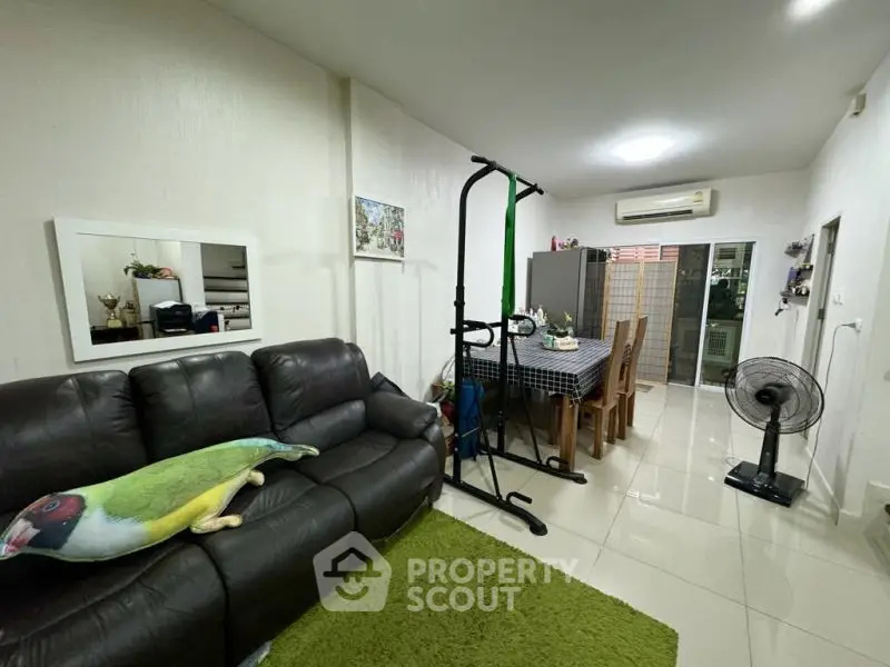 Spacious living room with modern decor and dining area, featuring leather sofa and air conditioning.