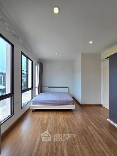 Spacious bedroom with large windows and wooden flooring in modern home